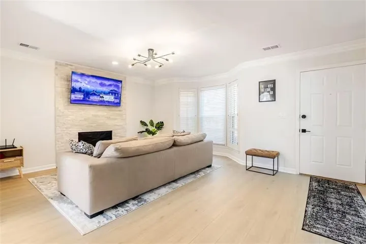 Light wood-finish flooring, a modern fireplace with stone-stacked surround, crown molding, and bay windows with plantation shutters