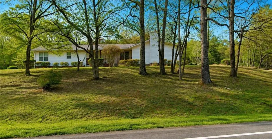 Ranch-style residence featuring a white exterior, a prominent chimney, and a gently sloping grassy front yard