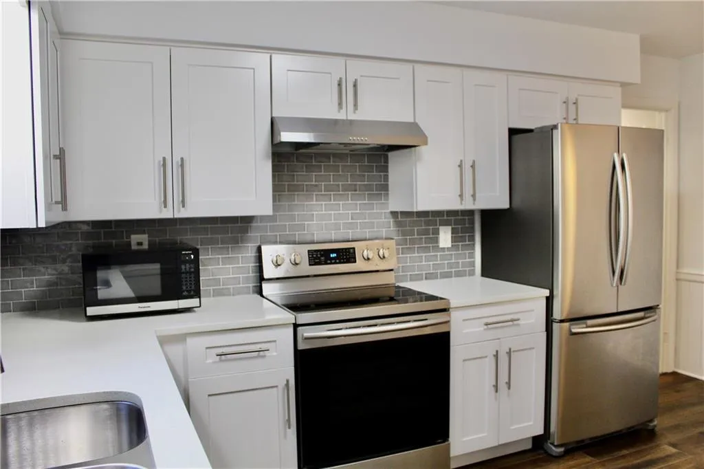 Kitchen with appliances with stainless steel finishes, under cabinet range hood, light countertops, white cabinets, and decorative backsplash