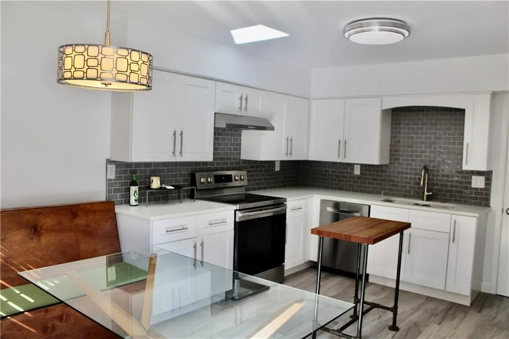 Kitchen with appliances with stainless steel finishes, under cabinet range hood, decorative backsplash, and light countertops