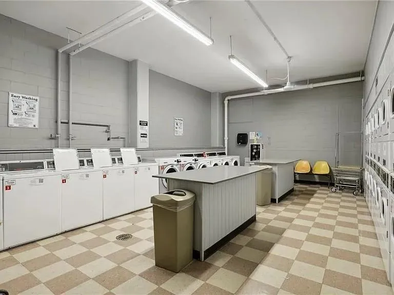 Community laundry room with light flooring, concrete block wall, and washer and clothes dryer