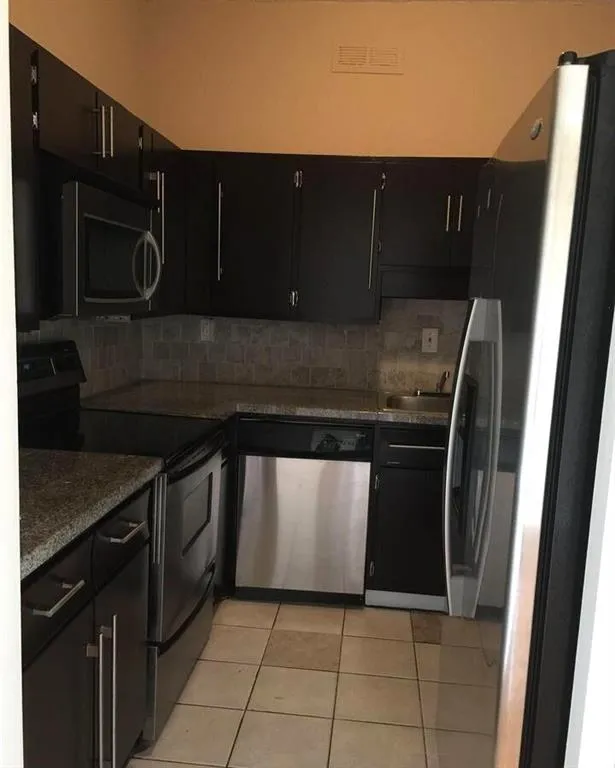 Kitchen with dark cabinets, stainless steel appliances, light tile patterned floors, and tasteful backsplash
