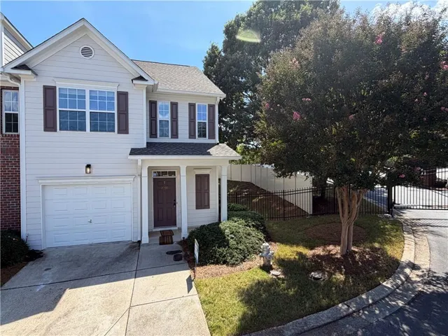 Attached garage with concrete driveway, light-toned siding, dark shutters, covered front entry, and black metal fencing