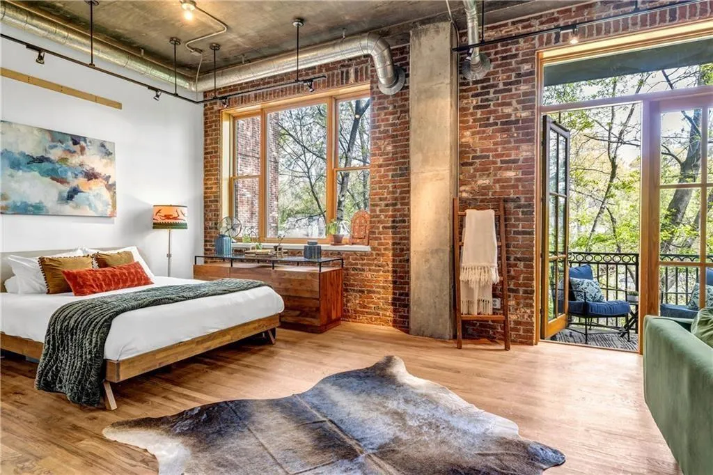 Bedroom with wood finished floors, access to outside, brick wall, a high ceiling, and multiple windows