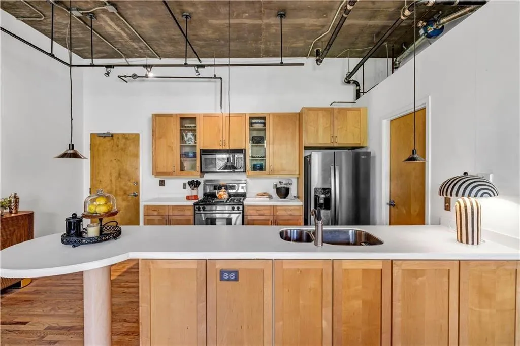 Kitchen with appliances with stainless steel finishes, a sink, a high ceiling, light countertops, and glass insert cabinets