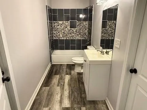 Full bathroom with wood-type flooring, tiled shower / bath, vanity, and toilet