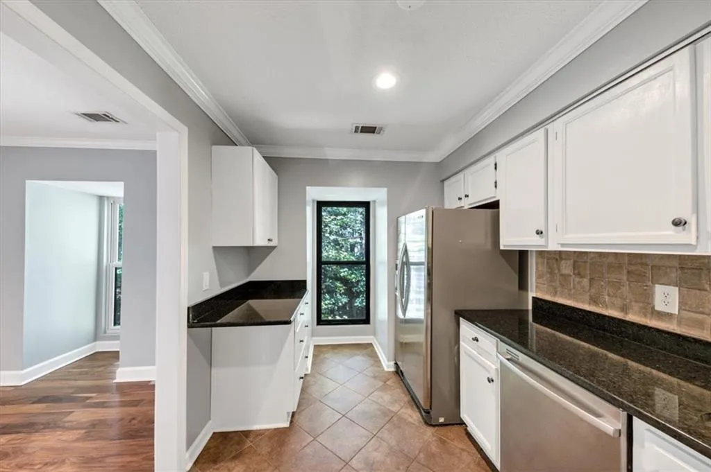 Kitchen with dark stone countertops, stainless appliances, ornamental molding, white cabinetry, and tasteful backsplash