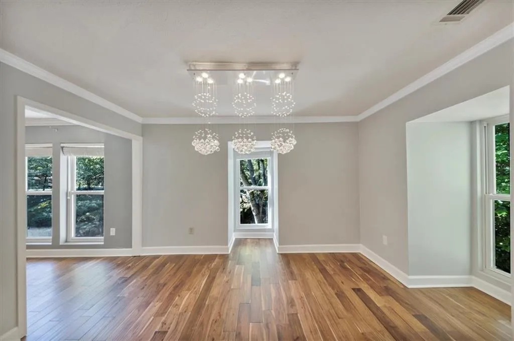 Unfurnished dining area featuring healthy amount of natural light, wood finished floors, crown molding, and a chandelier