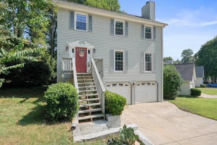 Two-story residence with light-colored siding, contrasting gray shutters, and a red entry door