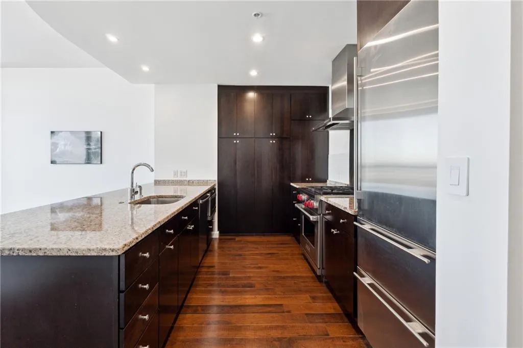 Kitchen with range hood, high end appliances, dark wood-type flooring, a sink, and a peninsula