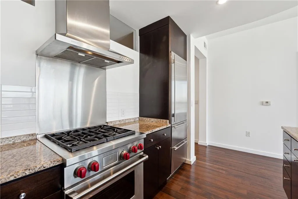 Kitchen featuring dark brown cabinetry, high end stainless steel range, backsplash, wall chimney exhaust hood, and dark wood finished floors