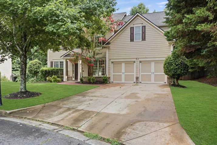 Two-story residence featuring light-colored siding, a dark roof, and a two-car garage with cream-colored doors