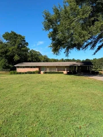 Brick exterior with an expansive front lawn, mature trees, and an attached carport