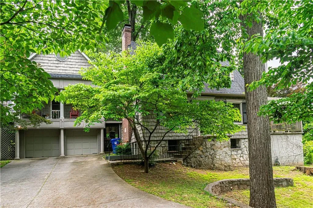 Obstructed view of property featuring driveway, an attached garage, a balcony, and a chimney