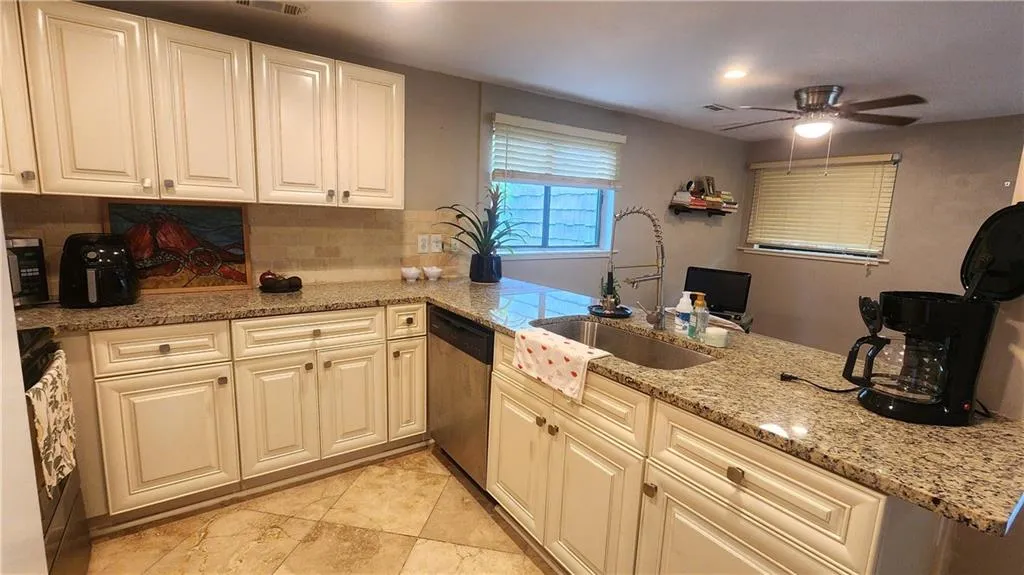 Kitchen with a sink, dishwasher, a ceiling fan, light stone counters, and backsplash