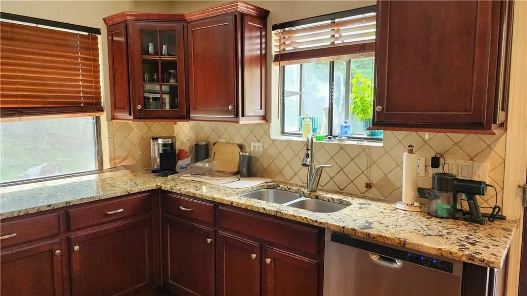 Kitchen featuring stainless steel dishwasher, a sink, glass insert cabinets, tasteful backsplash, and light stone countertops