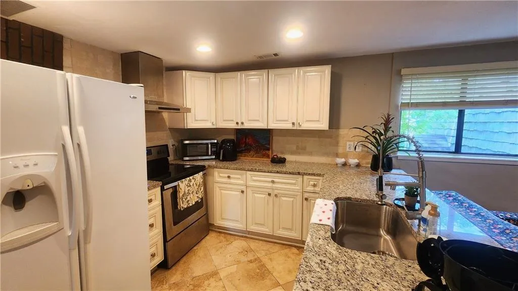 Kitchen featuring stainless steel appliances, a sink, under cabinet range hood, white cabinetry, and light stone counters