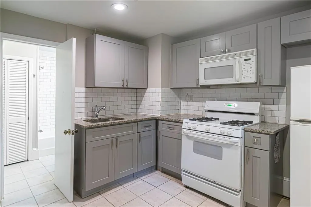 Kitchen with white appliances, gray cabinetry, light tile patterned floors, light stone counters, and recessed lighting