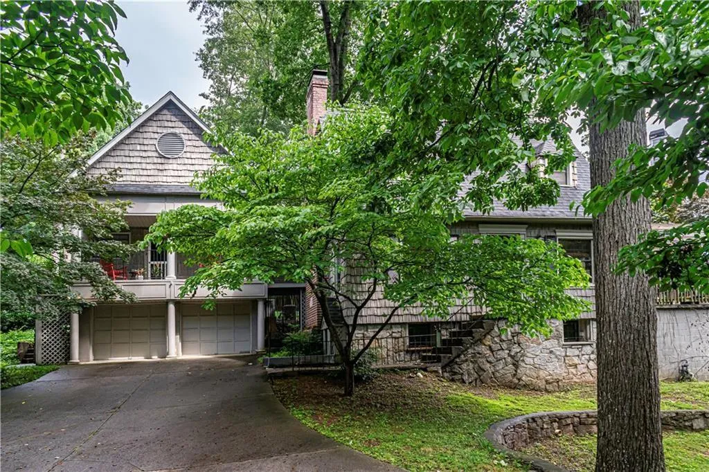 View of property hidden behind natural elements featuring an attached garage, stairs, driveway, and a chimney