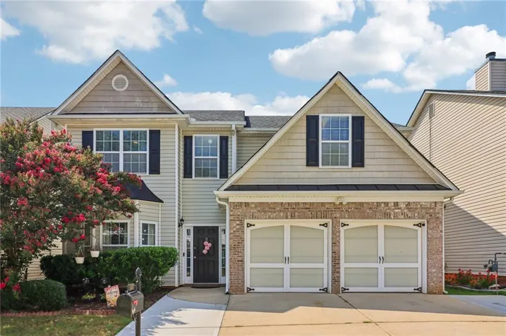 Light-colored siding exterior with brick accents, multi-pane windows with dark shutters, and a two-car garage