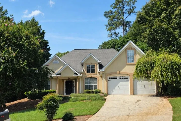 Stucco exterior with a gabled roofline, multiple dormer windows, a two-car garage, and established landscaping