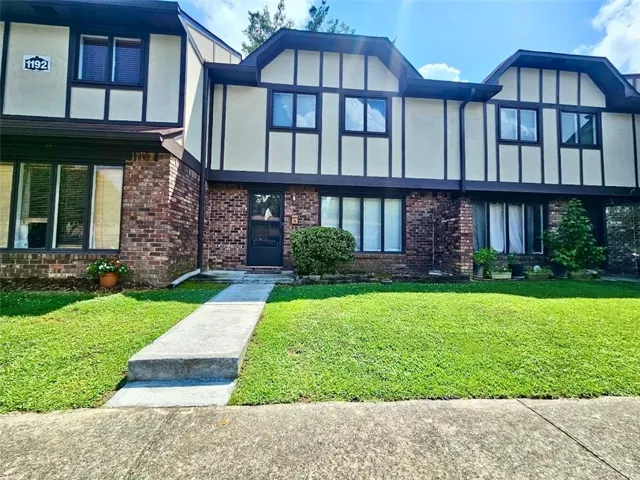 Brick and stucco exterior with dark trim, featuring a concrete walkway and a green lawn