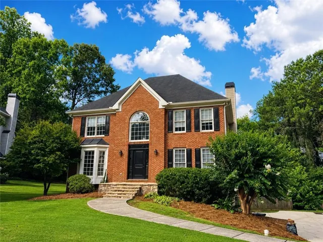Traditional brick exterior featuring a prominent arched window above the main entry, contrasting dark shutters, a bay window, and a dark shingle roof