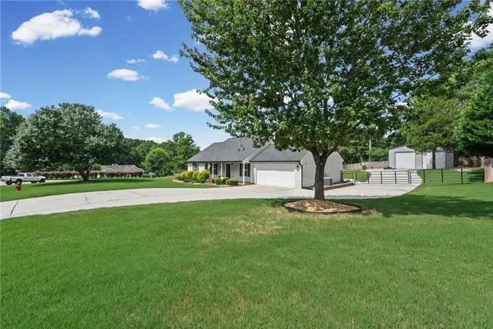 Ranch-style residence featuring a prominent front lawn, a long paved driveway, and mature landscaping