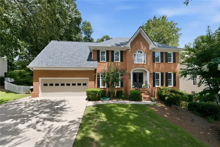Brick facade residence featuring a front entry with steps, a two-car garage, and mature landscaping