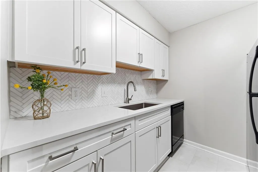Kitchen with white cabinetry, dishwasher, light stone counters, backsplash, and freestanding refrigerator