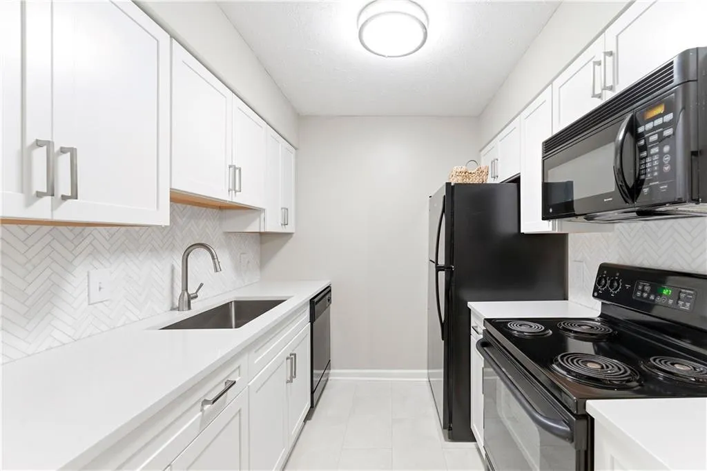 Kitchen with black appliances, white cabinetry, tasteful backsplash, and light stone countertops