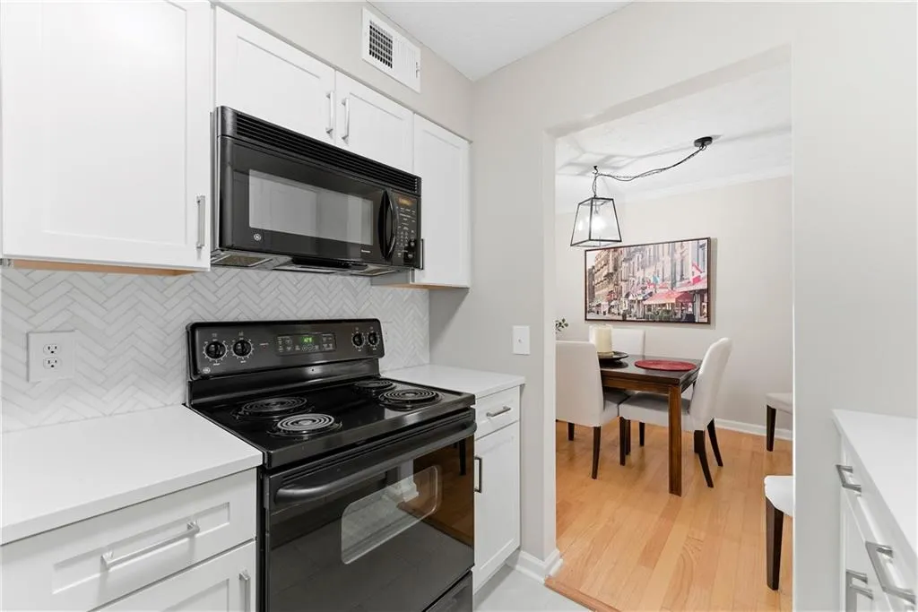 Kitchen featuring black appliances, white cabinets, decorative backsplash, ornamental molding, and light wood-style floors