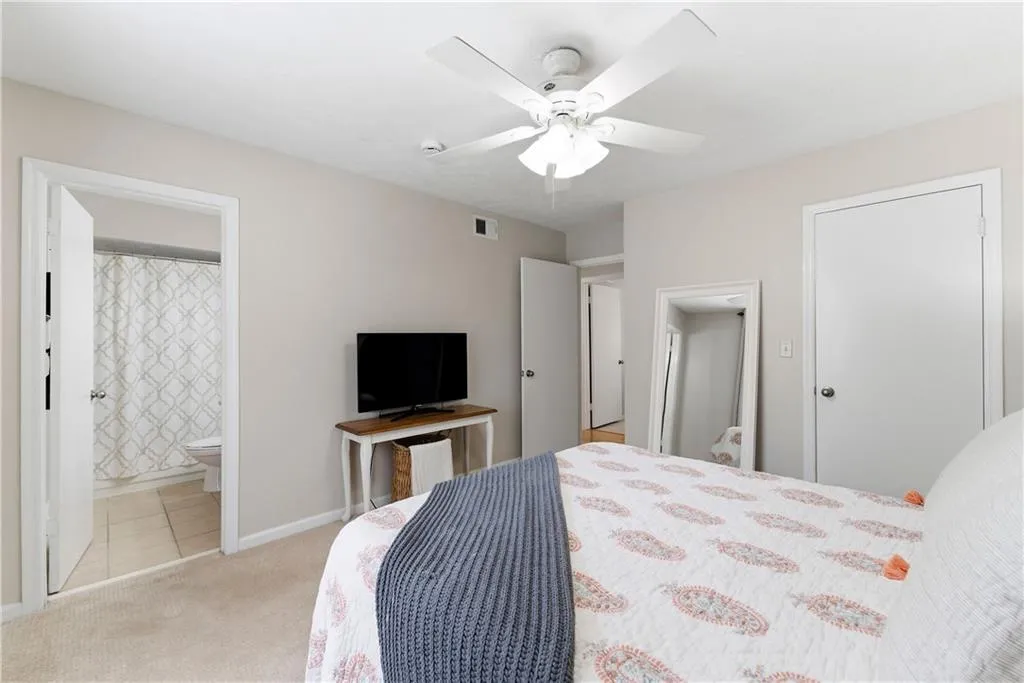 Bedroom with light colored carpet, a ceiling fan, and ensuite bathroom