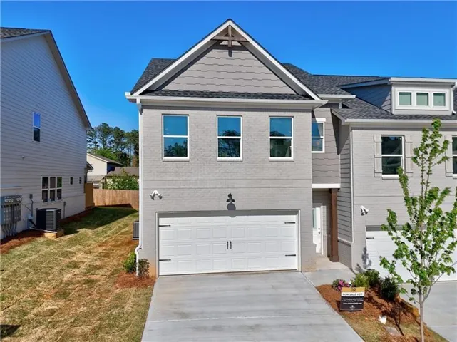 Contemporary townhouse exterior featuring a two-car garage, grey brick facade, and decorative gable siding