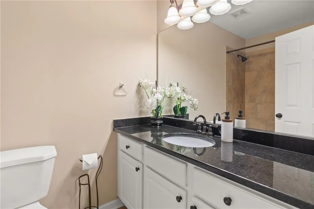 Bedroom 1's bathroom features beautiful black countertops, modern shower and tub combo, and a wide vanity with extensive cabinet and counter space