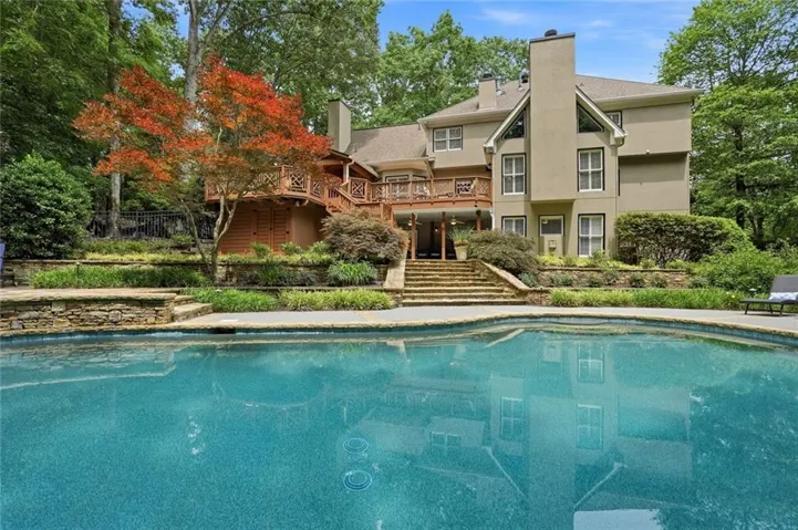 Expansive outdoor pool with stone coping, a stucco exterior, multiple outdoor decks, and a tiered stone retaining wall