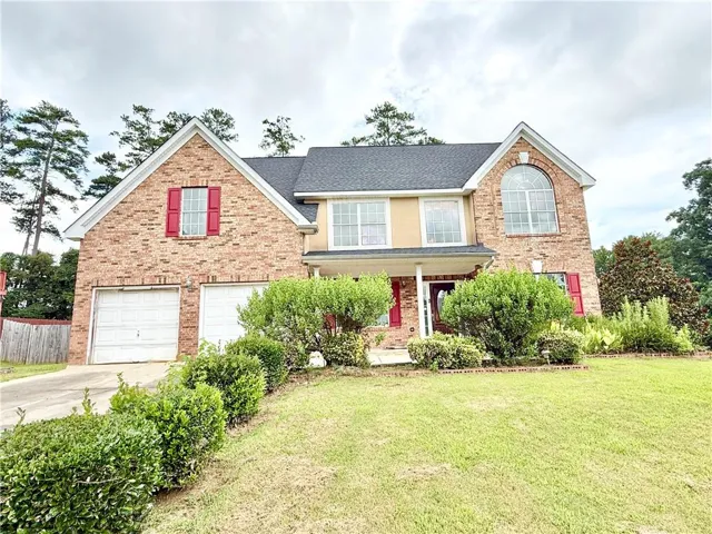Brick facade residence with a two-car garage, established front landscaping, and a prominent arched window feature