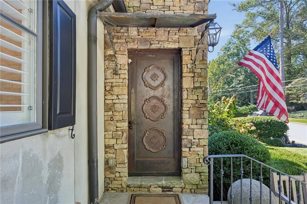Stone facade featuring a custom metal door with decorative molding, metal door canopy, and a wall-mounted lantern light fixture