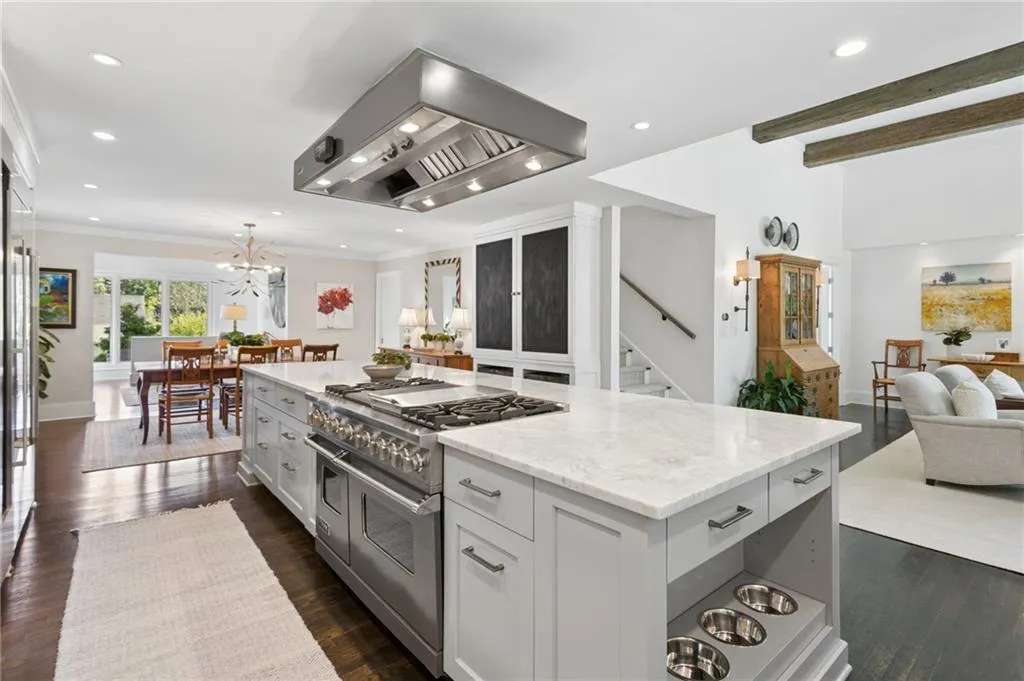 Kitchen island with stone countertop, large-scale stainless steel gas range, integrated stainless steel range hood, dark wood-finish flooring, and reclaimed wood ceiling beams