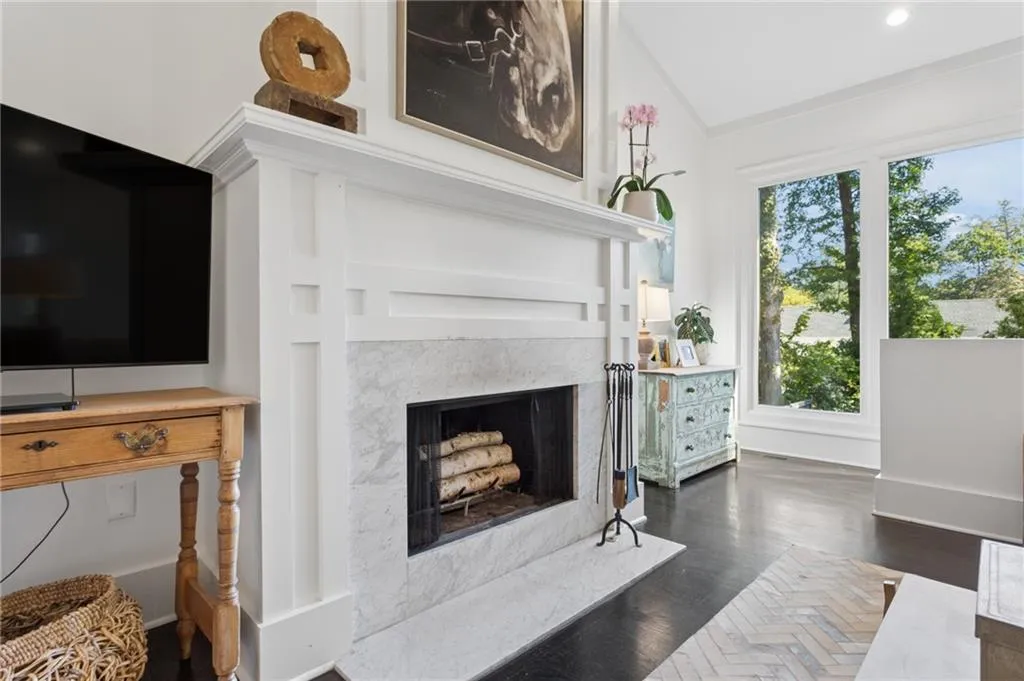 Wood burning fireplace with white millwork mantel, vaulted ceiling, and dark-toned wood-finish flooring
