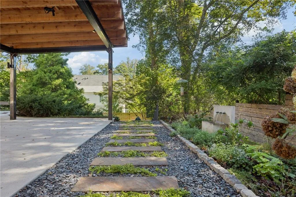 Carport featuring an exposed timber-beam ceiling, stone-slab walkway set in dark gravel, integrated stone water feature, and horizontal wood-slat fencing