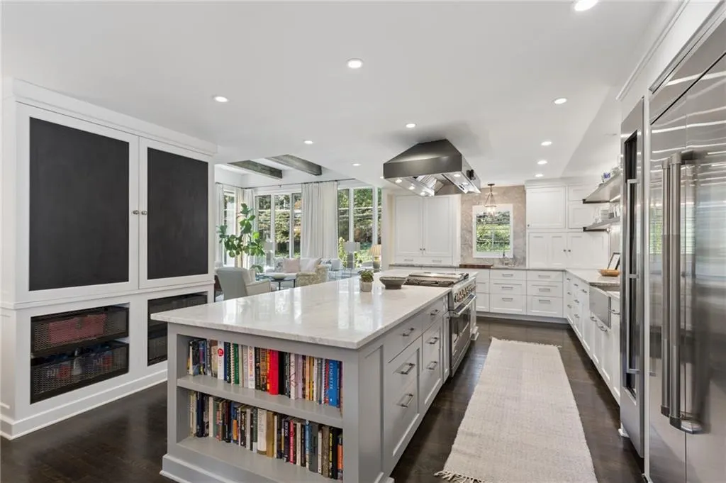 Gourmet kitchen featuring a large central island with integrated open shelving, stone countertops, stainless steel professional-grade range with overhead hood, custom cabinetry, and dark-toned wood flooring