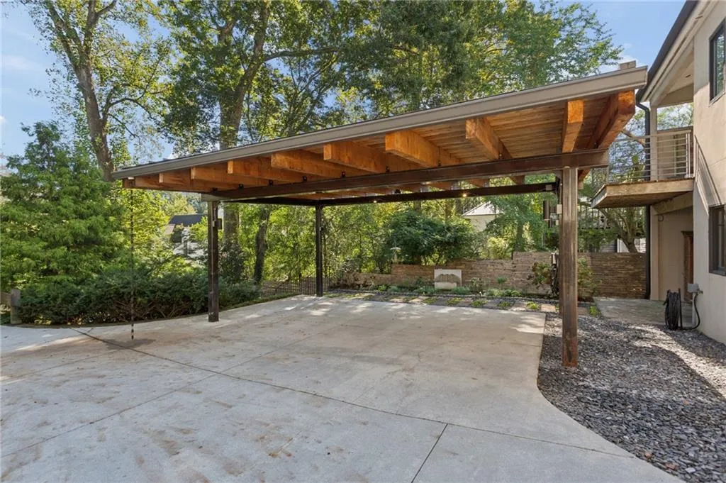 Covered carport featuring exposed timber beams, a metal roof structure, concrete parking surface, and metal support posts