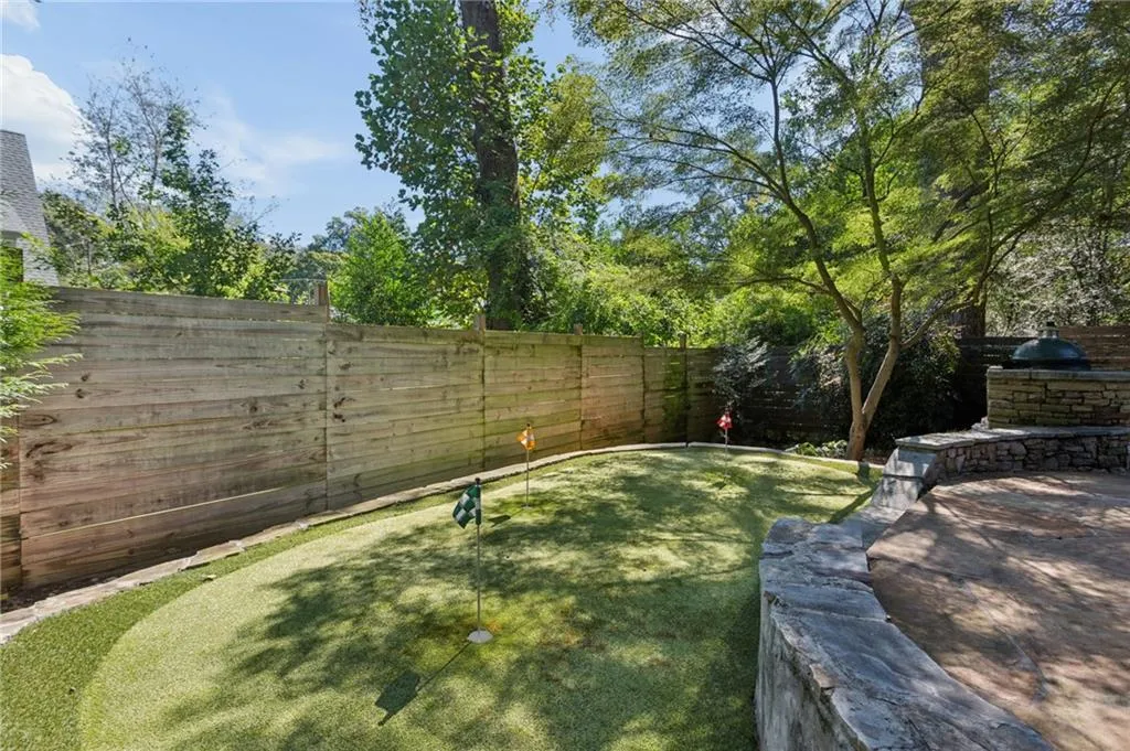 Backyard featuring a synthetic putting green, stacked stone retaining wall, paved patio area, and privacy fencing