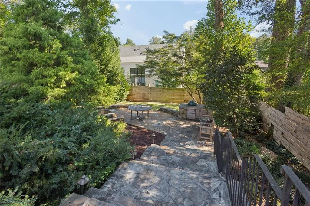 Flagstone patio featuring a built-in masonry grill station, stone-lined fire pit, custom metal railing, and privacy fencing