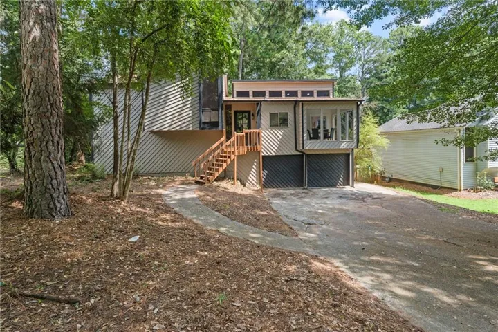 Multi-level residence featuring a wood deck entry, sunroom, two-car garage, and sloped driveway