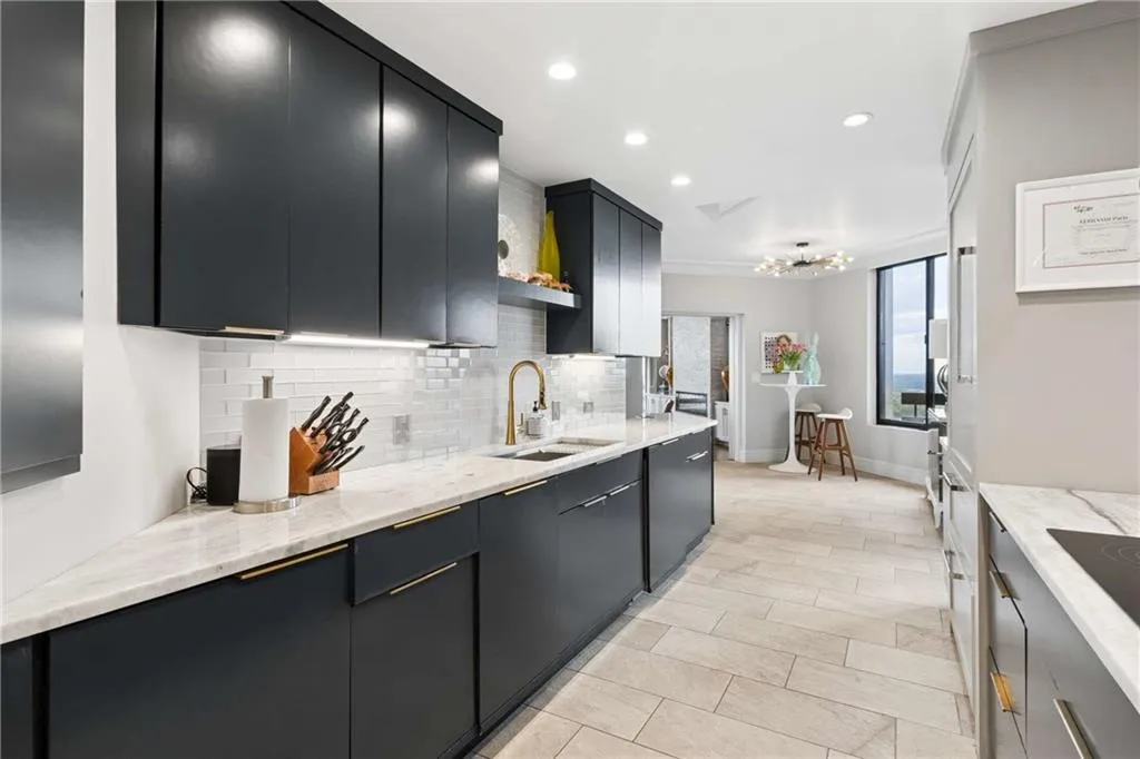 Kitchen with dark cabinets, light stone counters, decorative backsplash, a chandelier, and black electric cooktop