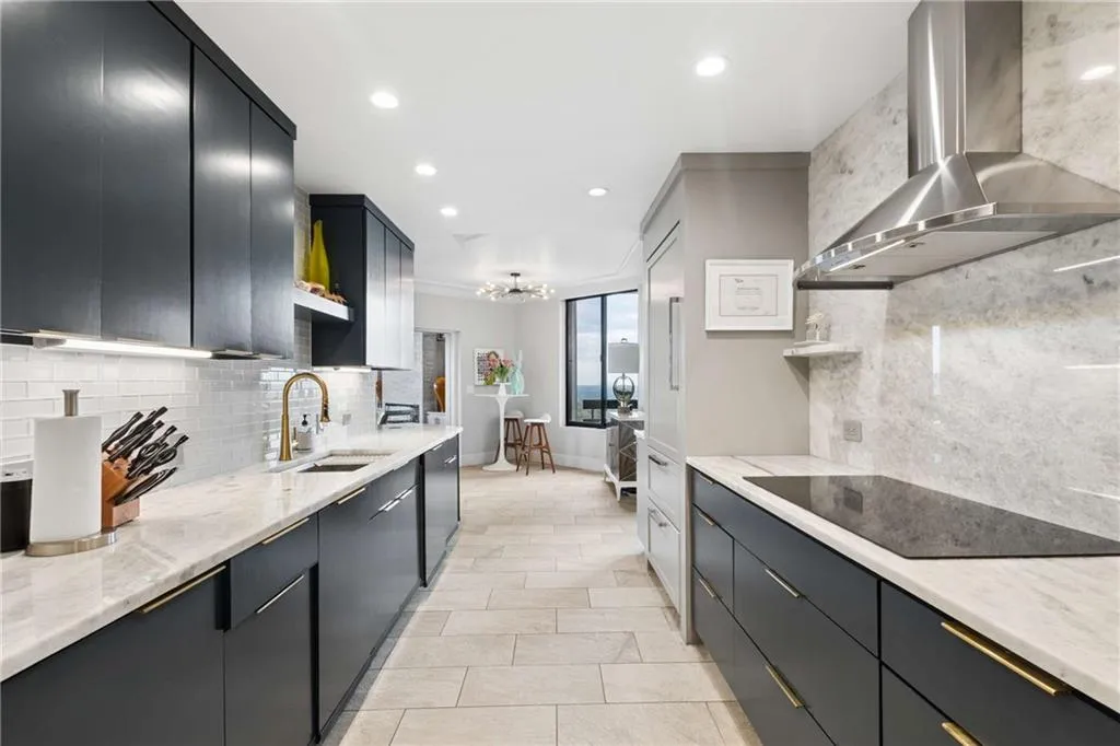 Kitchen with dark cabinetry, light stone countertops, black electric stovetop, hanging lights, and modern cabinets