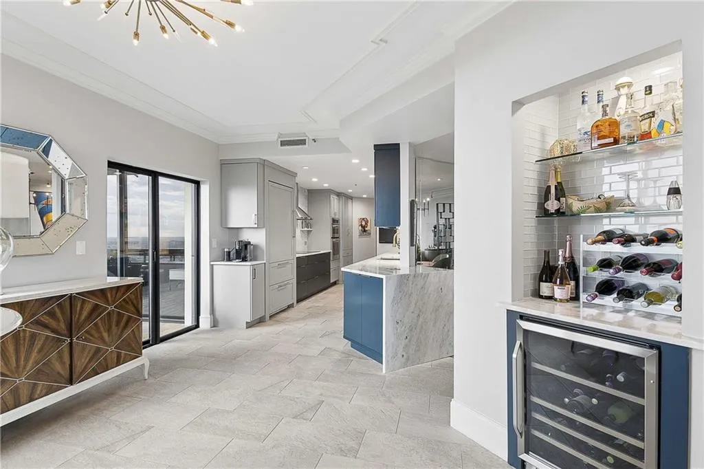 Bar area featuring beverage cooler, light stone counters, ornamental molding, a chandelier, and gray cabinetry