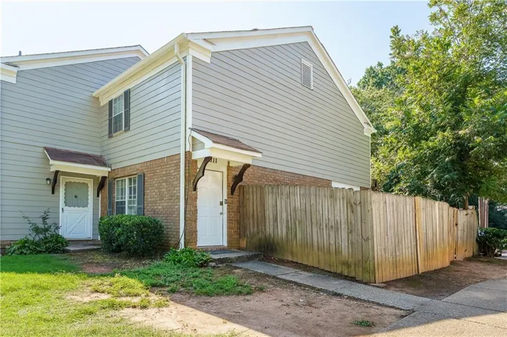 Two-story exterior featuring brick and horizontal siding, individual entry doors with awnings, and a privacy fence